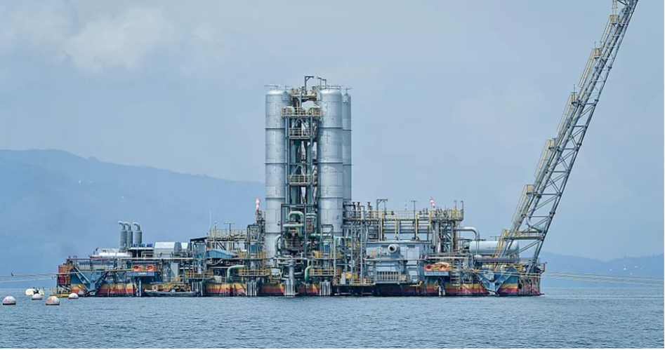 An industrial barge sits on top of a blue-grey lake with hazy mountains in the background. 